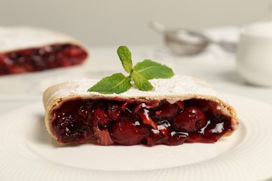 Photo of Delicious strudel with cherries, powdered sugar and mint on plate, closeup