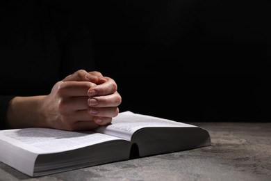 Religion. Christian woman praying over Bible at table against black background, closeup. Space for text