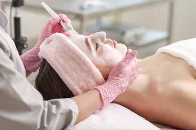 Photo of Cosmetologist applying mask on woman's face in clinic, closeup