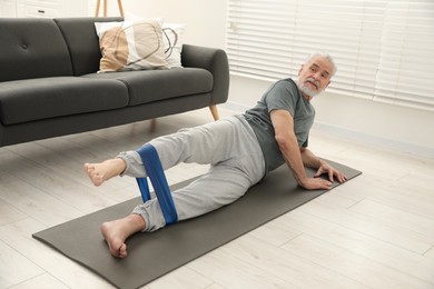 Photo of Senior man doing exercise with fitness elastic band on mat at home