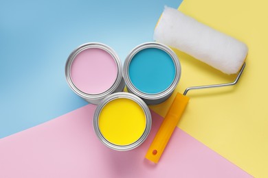 Cans with different paints and roller on color background, flat lay