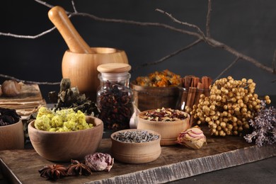 Photo of Many different dry herbs, flowers and mortar with pestle on black table