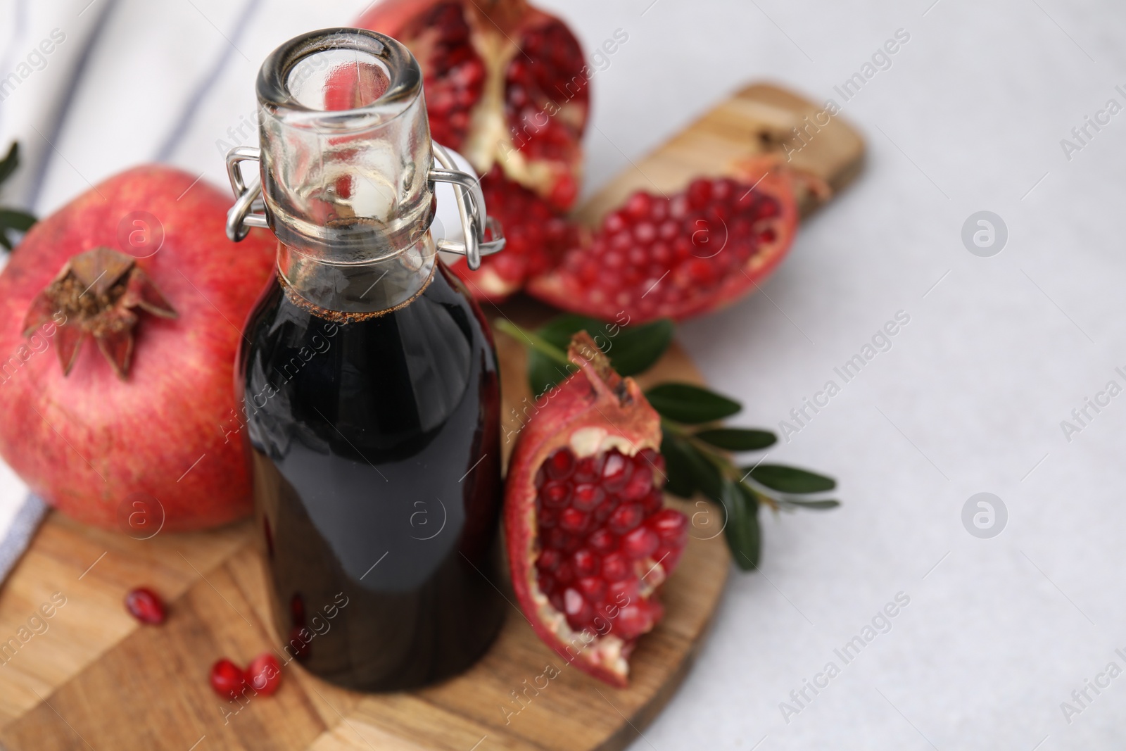 Photo of Tasty pomegranate sauce in bottle, branch and fruits on light table, closeup. Space for text