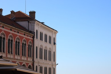 Photo of Exterior of buildings with arched windows against blue sky. Space for text