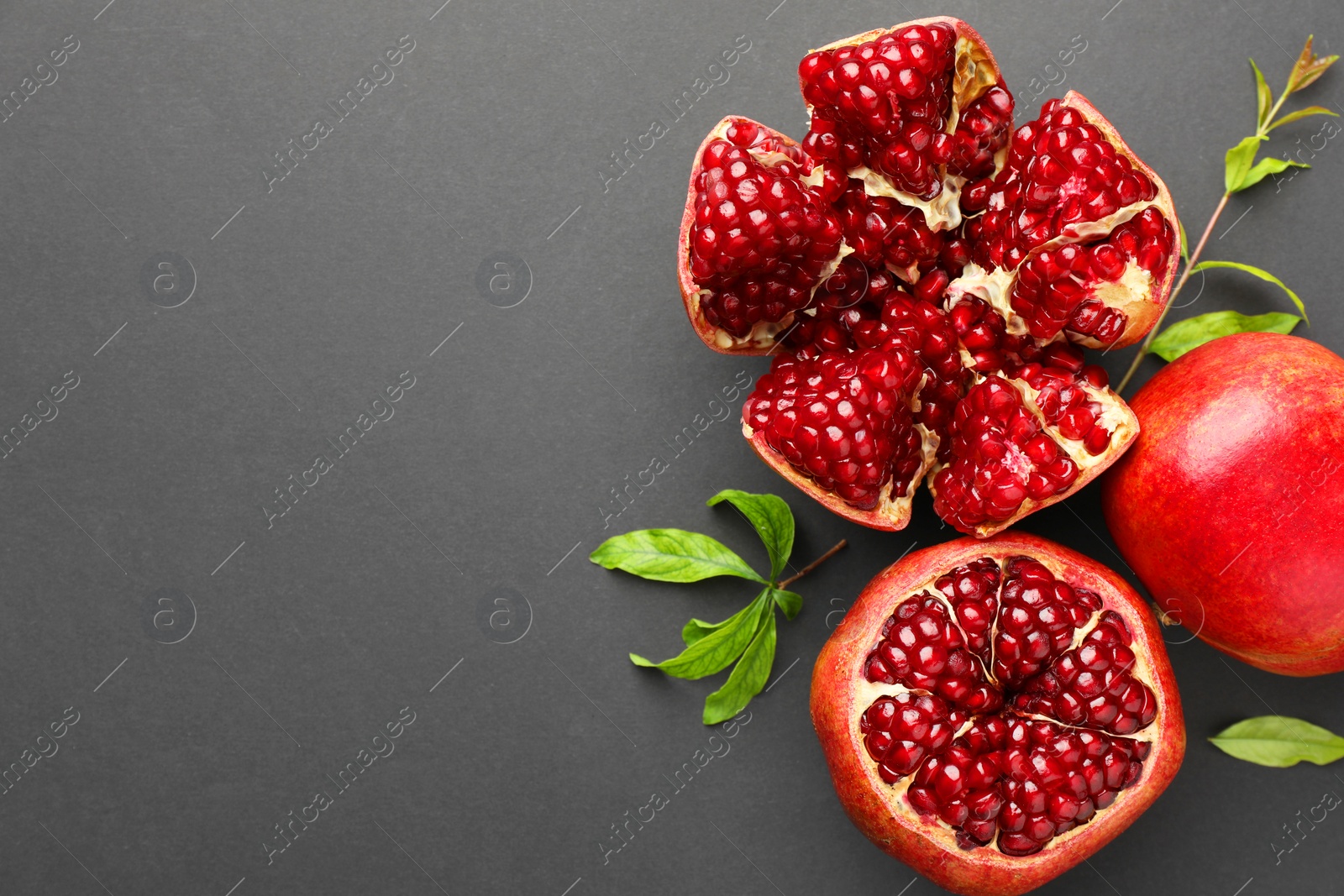 Photo of Fresh ripe pomegranates and leaves on grey background, top view. Space for text
