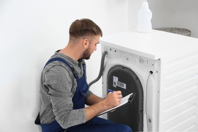 Photo of Young plumber with clipboard near washing machine in bathroom