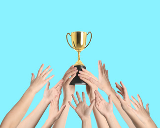 People with golden trophy cup on turquoise background, closeup