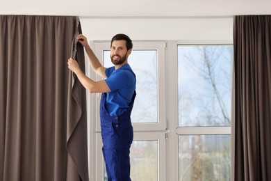 Photo of Worker in uniform hanging window curtain indoors