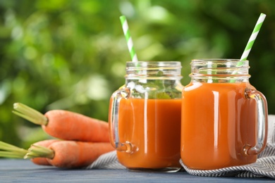 Photo of Mason jars of tasty drink and carrots on table against blurred background, space for text