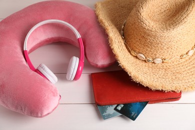 Photo of Pink travel pillow, hat, headphones and wallet with credit cards on white wooden background, above view