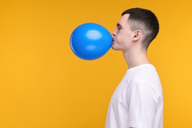 Photo of Young man inflating light blue balloon on yellow background. Space for text