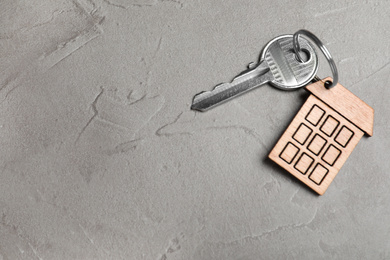 Photo of Key with trinket in shape of house on grey stone background, top view and space for text. Real estate agent services