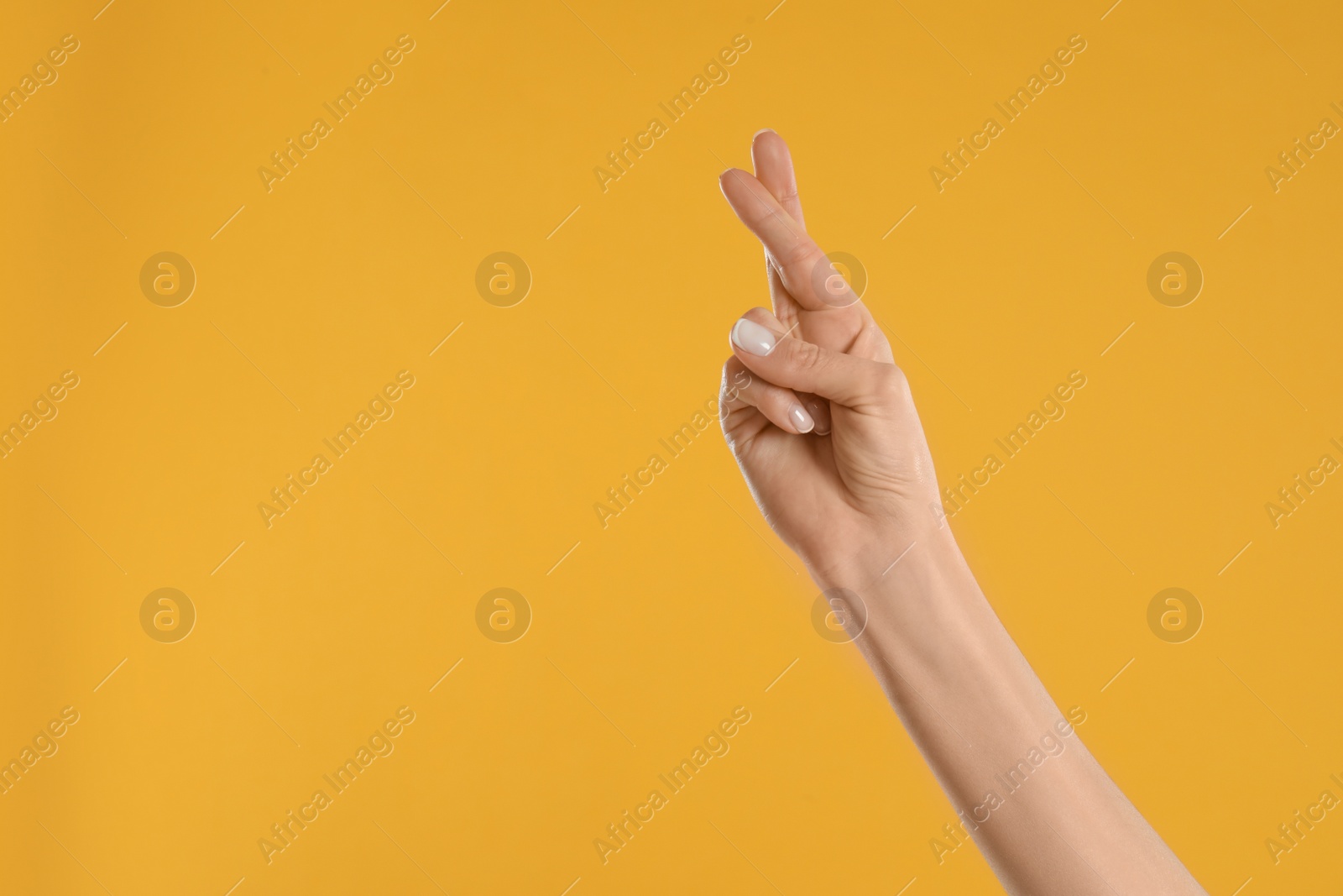 Photo of Woman with crossed fingers and space for text on yellow background, closeup. Superstition concept