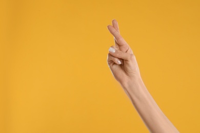 Photo of Woman with crossed fingers and space for text on yellow background, closeup. Superstition concept