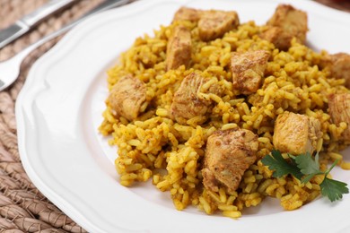 Plate of delicious rice with chicken on wicker mat, closeup