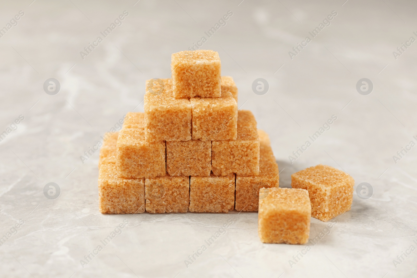 Photo of Pyramid made of brown sugar cubes on light grey marble table, closeup