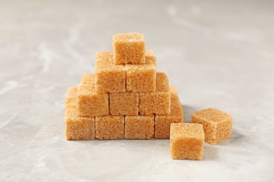 Photo of Pyramid made of brown sugar cubes on light grey marble table, closeup