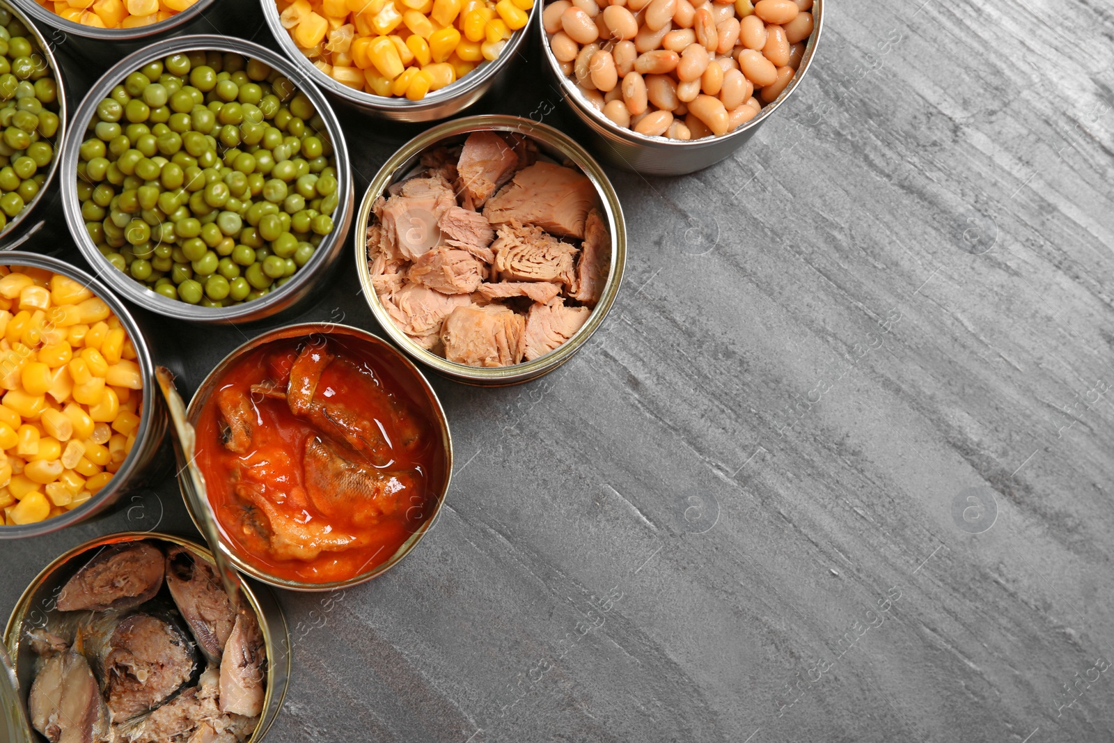 Photo of Open tin cans of conserved products on grey table, flat lay with space for text