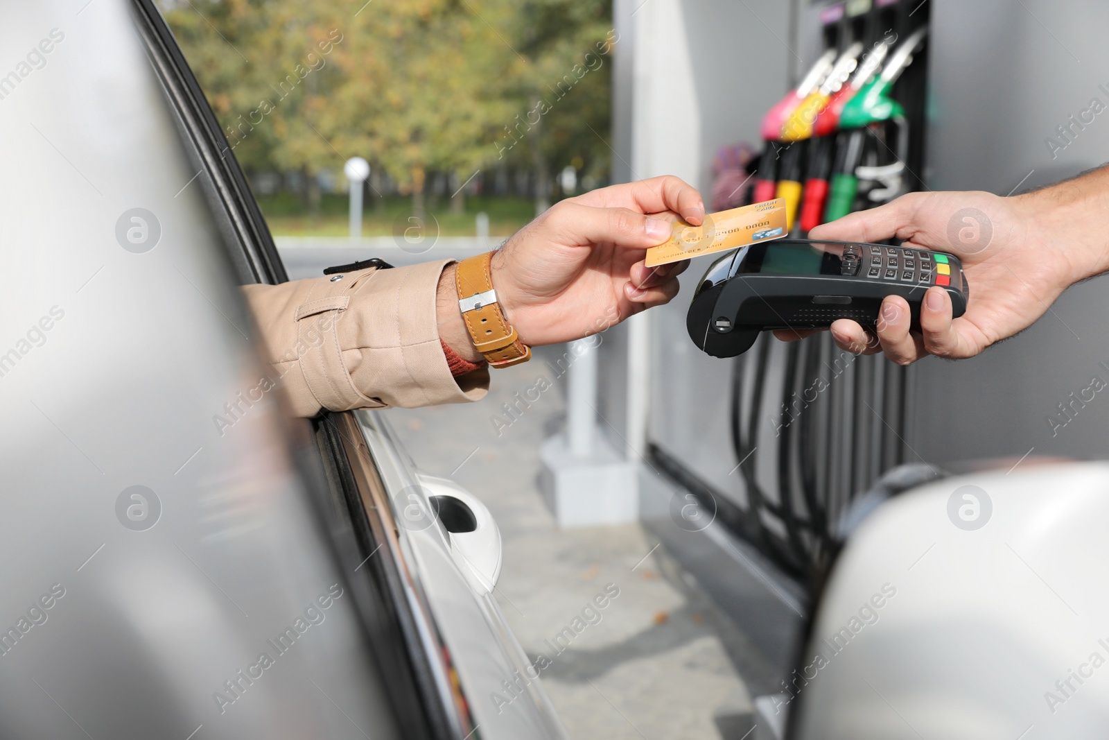 Photo of Man sitting in car and paying with credit card at gas station, closeup