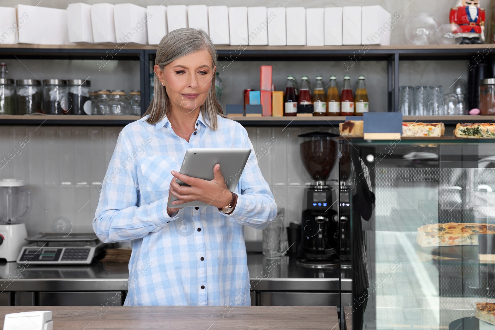 Photo of Business owner using tablet at cashier desk in her cafe