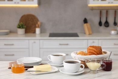 Photo of Breakfast served in kitchen. Fresh croissants, coffee, butter, jam, honey and sweetened condensed milk on white table