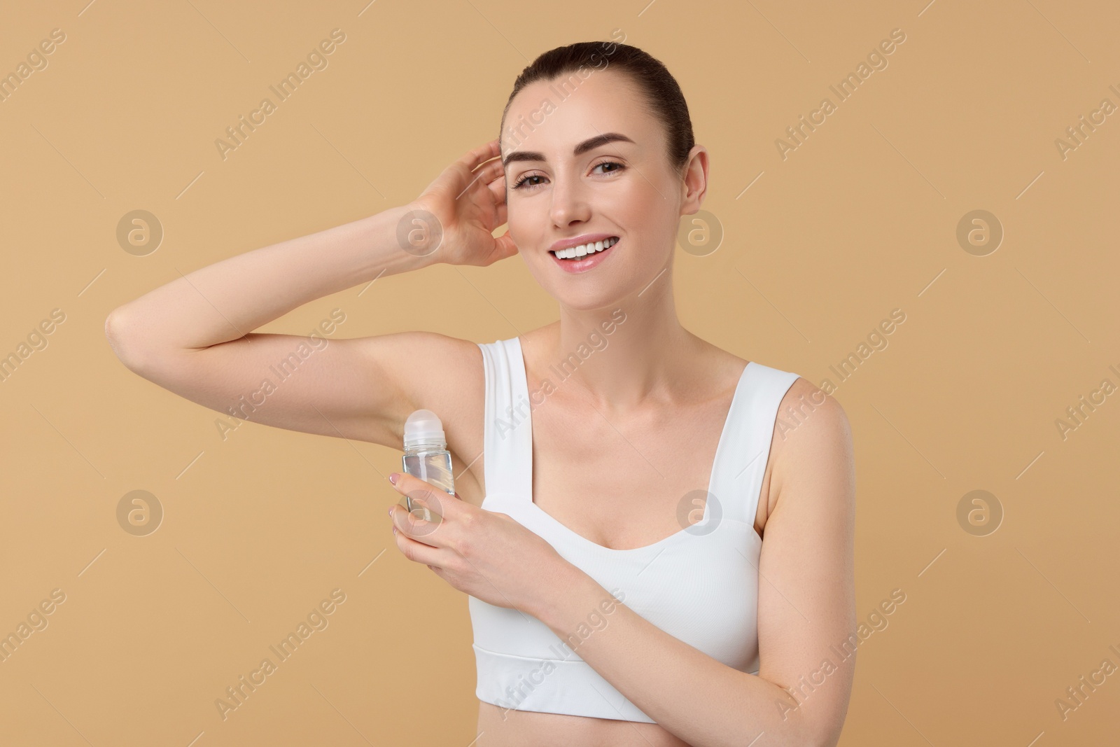 Photo of Beautiful woman applying deodorant on beige background