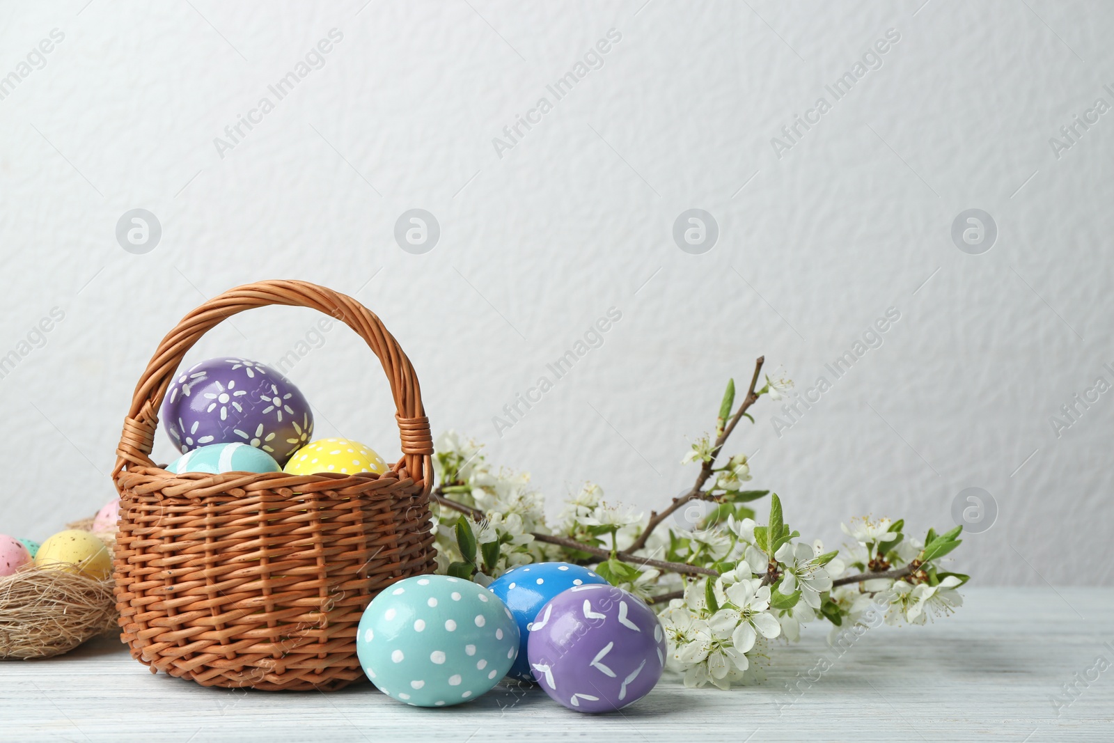 Photo of Composition with painted Easter eggs and blossoming branches on table. Space for text