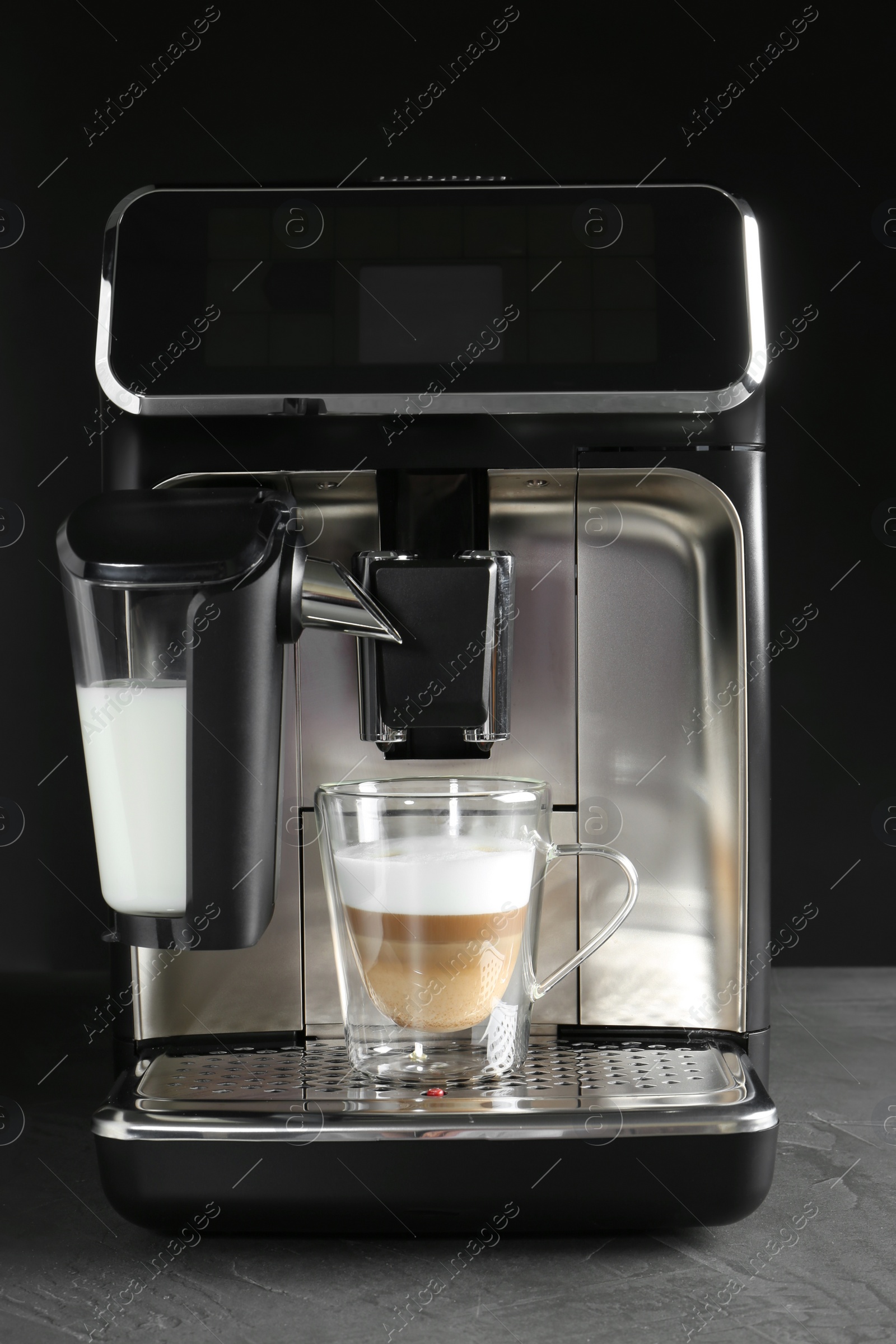 Photo of Modern coffee machine with glass cup of latte on grey table against black background