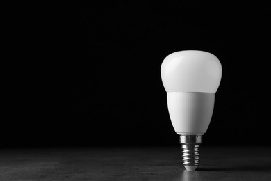 Photo of New modern lamp bulb on table against black background. Space for text