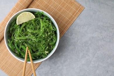 Photo of Tasty seaweed salad in bowl served on gray table, top view. Space for text