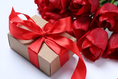 Beautiful gift box with bow and red tulip flowers on white background, closeup