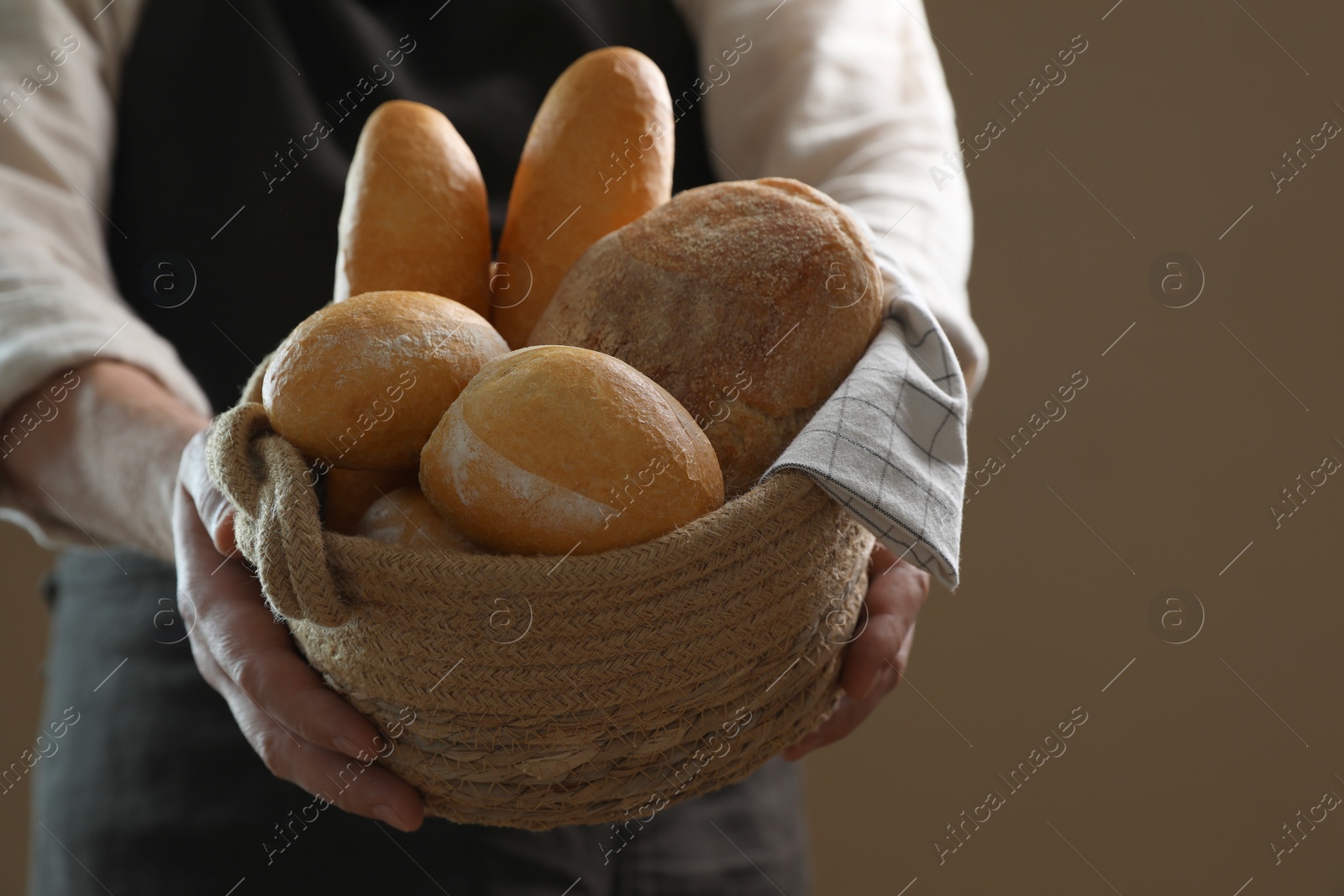 Photo of Man holding wicker basket with different types of bread on brown background, closeup