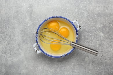 Photo of Whisk and eggs in pot on grey table, top view