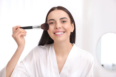 Beautiful young woman applying makeup with brush at home