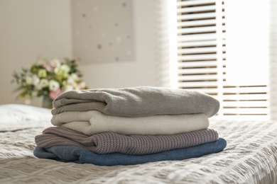 Stack of knitted sweaters on bed indoors