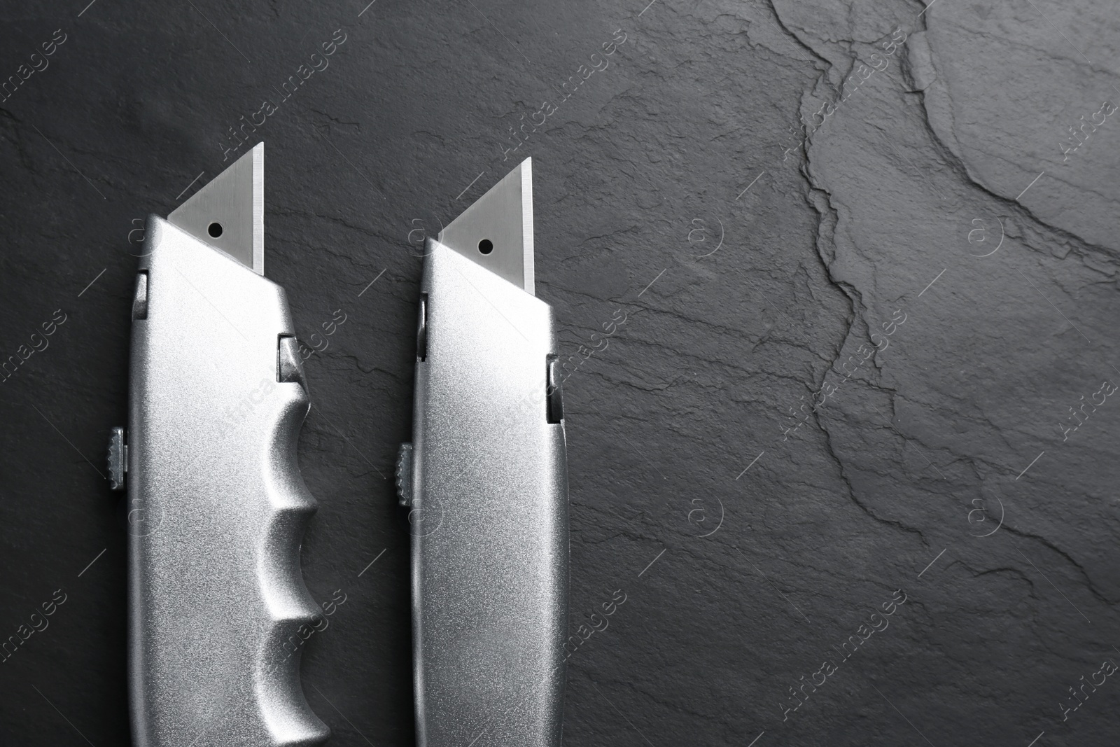 Photo of Two utility knives on black table, flat lay. Space for text