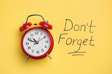 Photo of Alarm clock and text Don't forget on yellow background, top view. Reminder concept