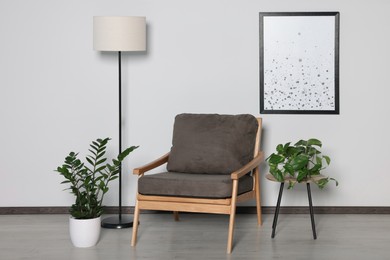 Stylish armchair, floor lamp and plants near white wall. Interior design