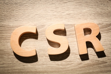 Abbreviation CSR made of wooden letters on table, flat lay. Corporate social responsibility