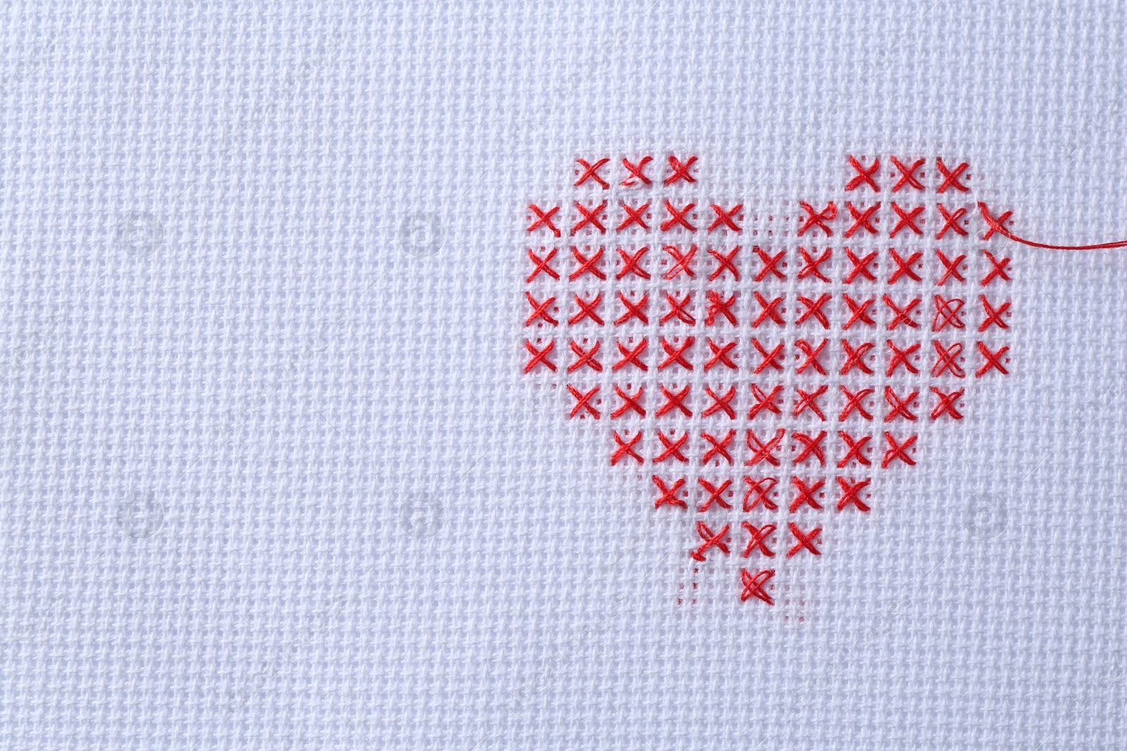 Photo of Embroidered red heart on white cloth, top view. Space for text