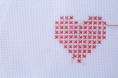 Embroidered red heart on white cloth, top view. Space for text