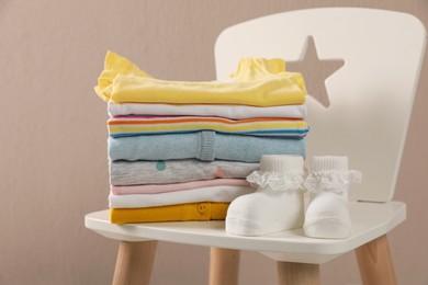 Stack of baby clothes and booties on chair near beige wall