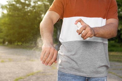 Photo of Man applying insect repellent on arm in park, closeup. Tick bites prevention