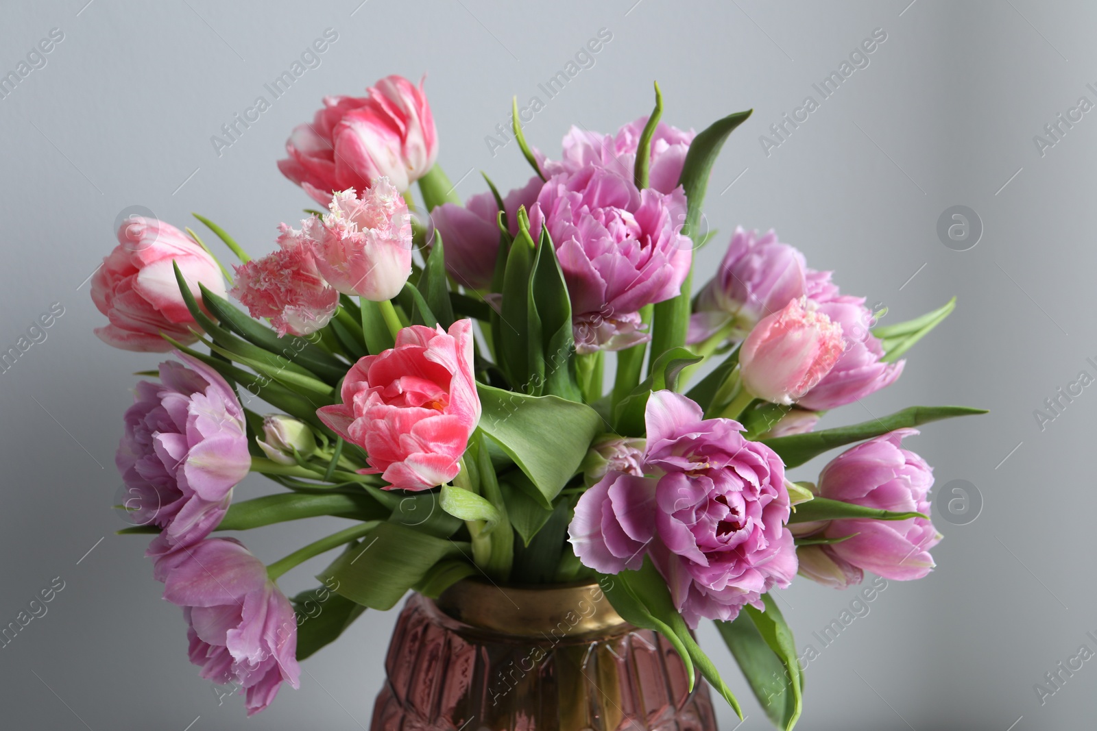 Photo of Beautiful bouquet of colorful tulip flowers near light grey wall, closeup