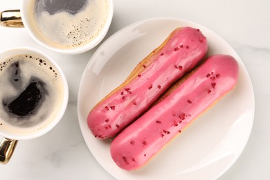 Tasty glazed eclairs and cups of coffee on white marble table, flat lay