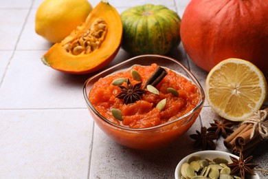 Photo of Bowl of delicious pumpkin jam and ingredients on tiled surface