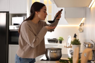 Photo of Beautiful woman with ladle tasting soup in kitchen