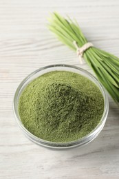 Photo of Wheat grass powder in glass bowl and fresh sprouts on white wooden table, closeup