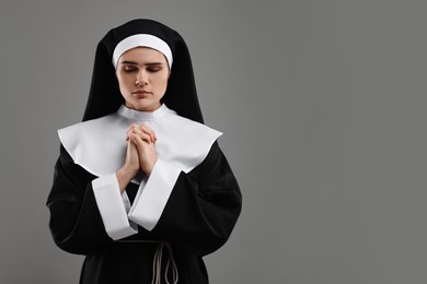 Photo of Nun with clasped hands praying to God on grey background. Space for text