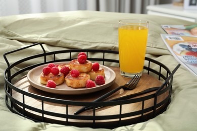 Photo of Tasty breakfast served in bedroom. Cottage cheese pancakes with fresh raspberries and juice on tray